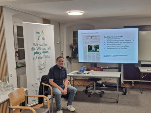 Ein Mann sitzt auf einem Stuhl in einem Raum vor einer Leinwand.